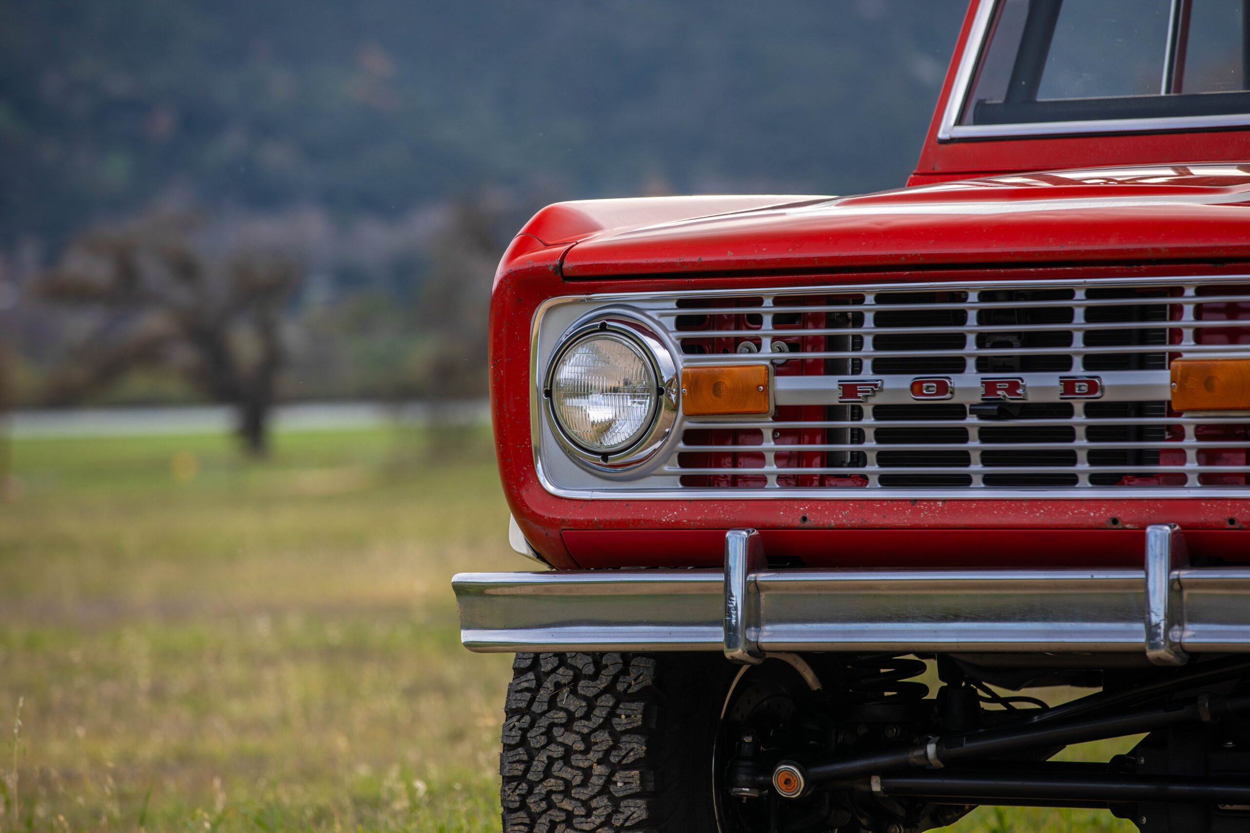 Front grille and headlight of a red vintage Ford Bronco outdoors.